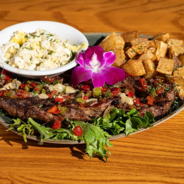 Grilled steak with peppers, onions, and sauce, served with roasted potatoes and potato salad.