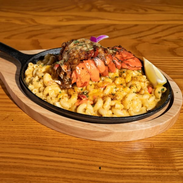 Lobster mac and cheese in a cast iron skillet on a wooden board with a lemon wedge.