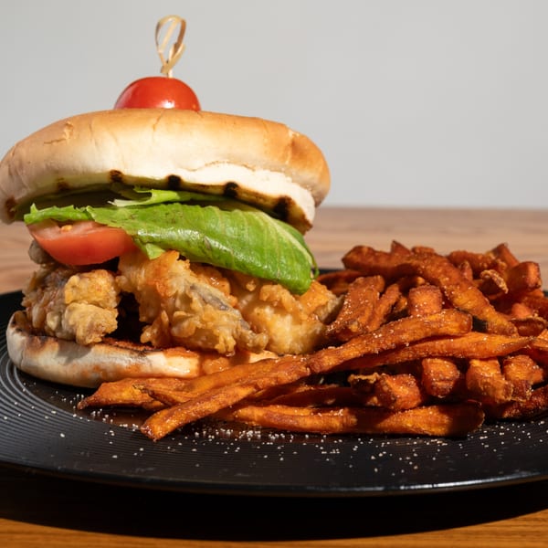 Crispy fried chicken sandwich with lettuce, tomato, and a side of sweet potato fries.