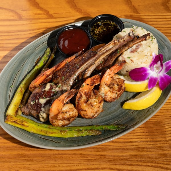 Grilled lamb chops and shrimp with mashed potatoes, asparagus, lemon wedges, and dipping sauces.